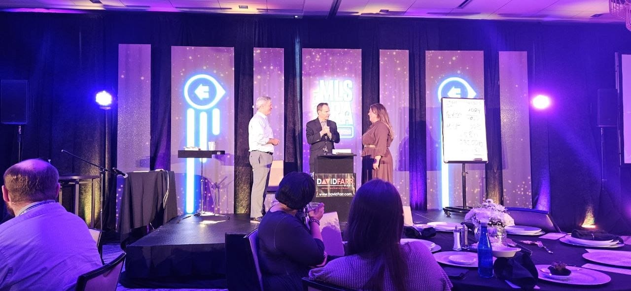 David Farr performing a stage magic show with two audience volunteers at a Minneapolis corporate banquet