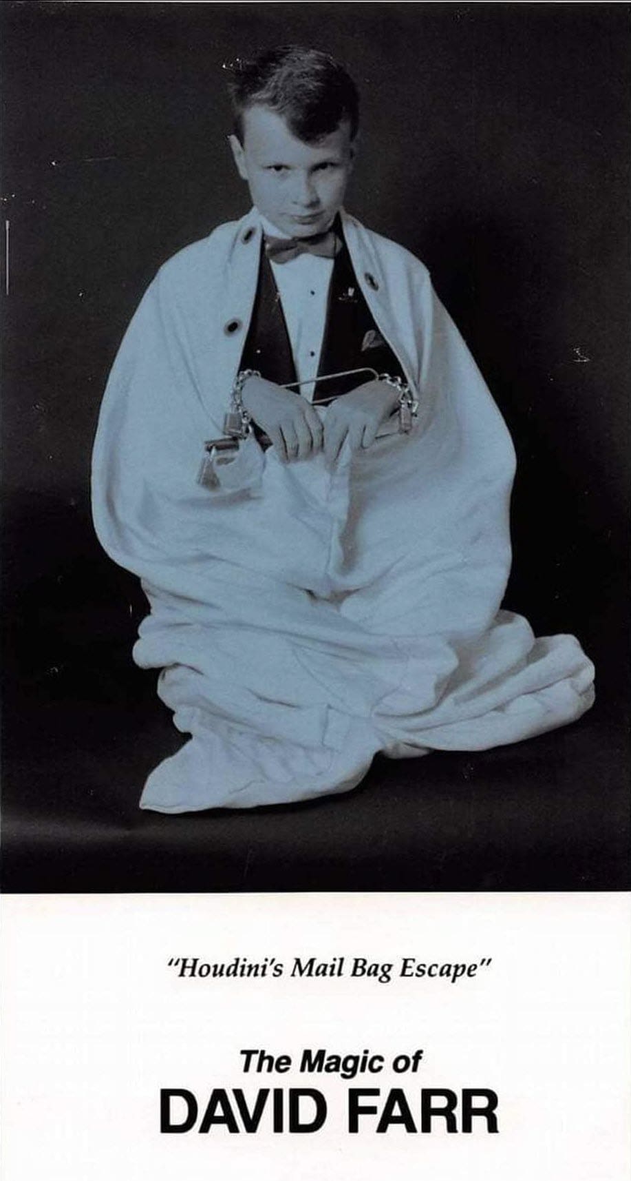 A young David Farr in a bow tie locked inside a canvas mail bag, performing Houdini's Mail Bag Escape on a promotional card